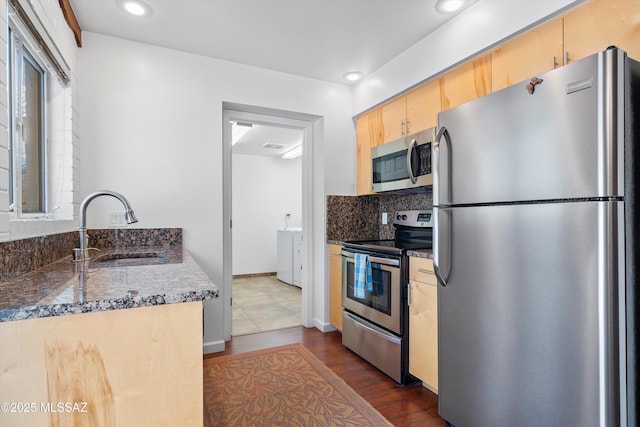 kitchen featuring light brown cabinetry, a sink, backsplash, appliances with stainless steel finishes, and dark wood-style flooring