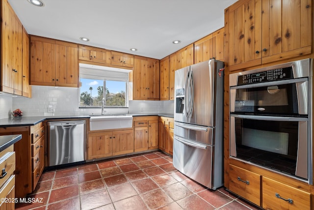 kitchen featuring recessed lighting, a sink, appliances with stainless steel finishes, dark countertops, and tasteful backsplash