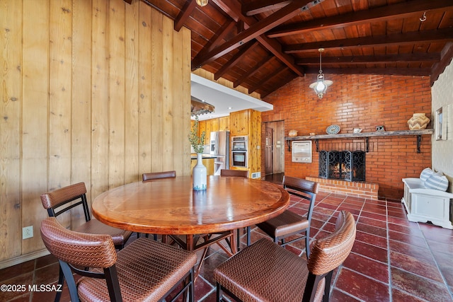 dining space featuring lofted ceiling with beams, a brick fireplace, wooden ceiling, and wood walls