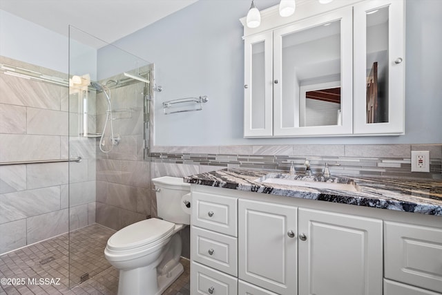 full bath featuring vanity, a stall shower, wainscoting, tile walls, and toilet