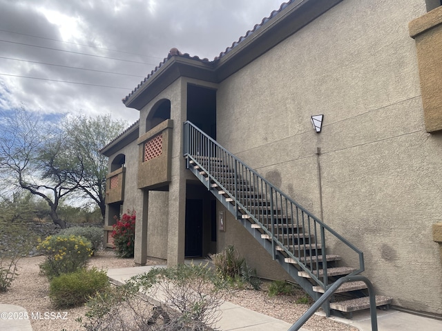 view of property exterior with stucco siding, stairs, and a tiled roof