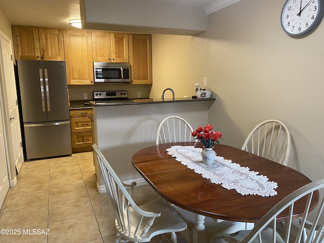 kitchen with light tile patterned flooring, a sink, stainless steel appliances, crown molding, and dark countertops