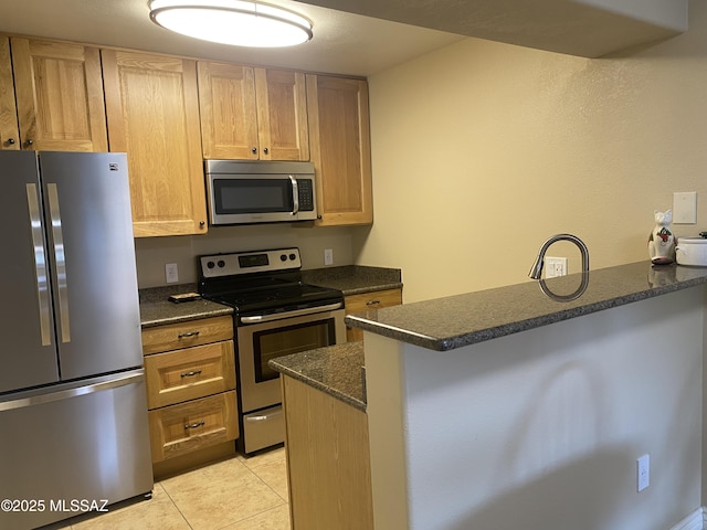 kitchen with dark stone countertops, light tile patterned floors, a peninsula, stainless steel appliances, and a kitchen breakfast bar