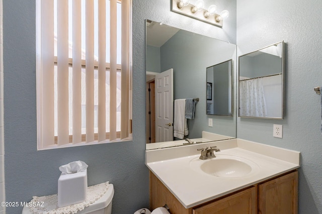 bathroom featuring a textured wall, vanity, and toilet