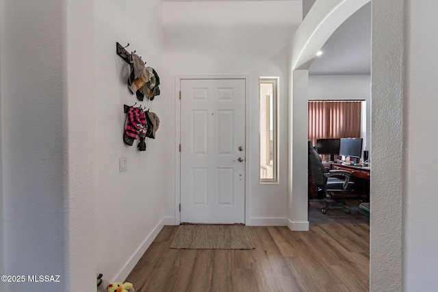 foyer with arched walkways, baseboards, and wood finished floors