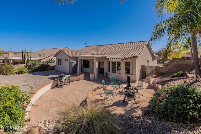 rear view of house with a tile roof, a gate, fence, a patio area, and stucco siding