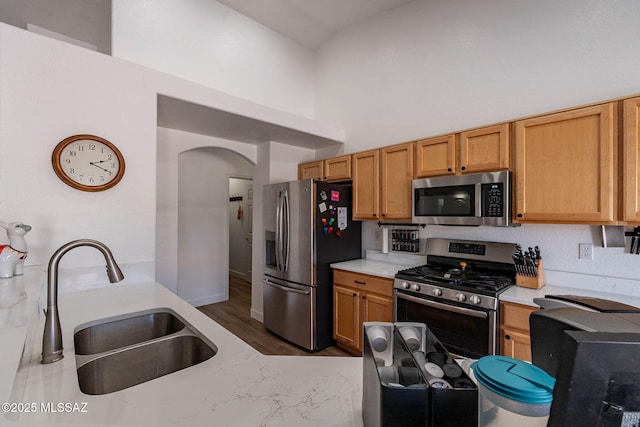 kitchen with arched walkways, a sink, a towering ceiling, light countertops, and appliances with stainless steel finishes