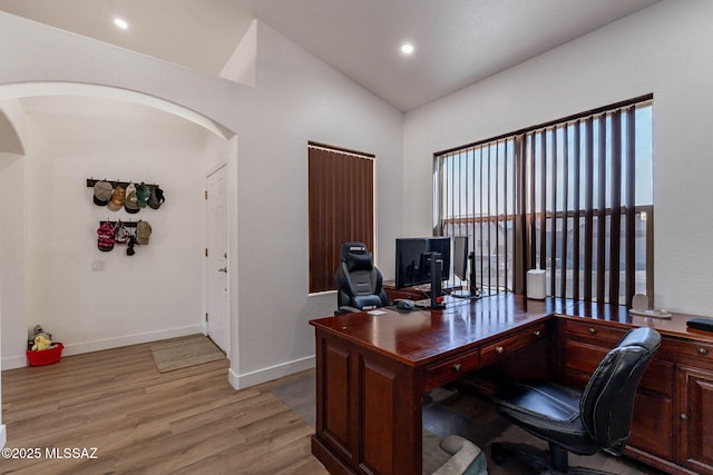 office featuring arched walkways, vaulted ceiling, light wood-style flooring, and baseboards