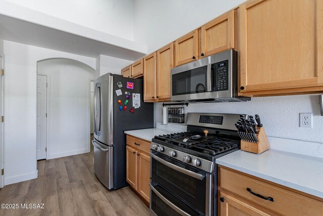 kitchen featuring arched walkways, stainless steel appliances, wood finished floors, baseboards, and light countertops