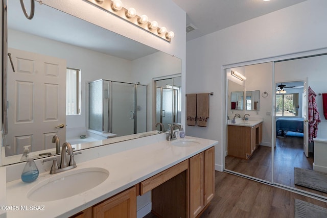 full bathroom with double vanity, a shower stall, a sink, and wood finished floors