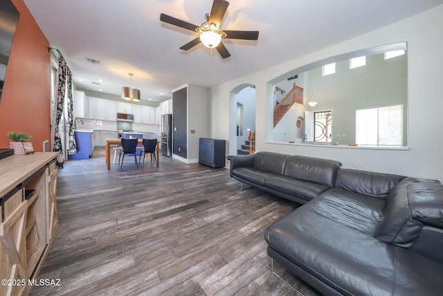 living area with ceiling fan, dark wood-type flooring, and arched walkways