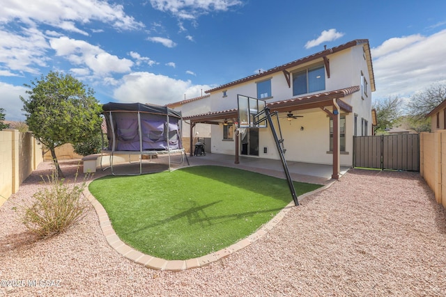 back of property with a ceiling fan, a trampoline, a patio area, stucco siding, and a fenced backyard