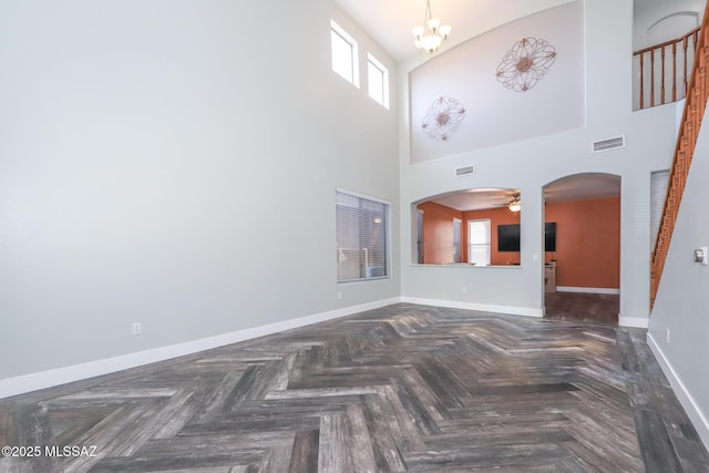 unfurnished living room with arched walkways, baseboards, visible vents, and ceiling fan with notable chandelier