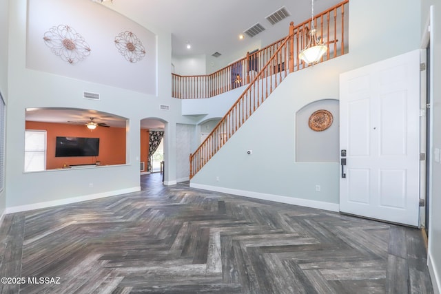 unfurnished living room with a ceiling fan, baseboards, visible vents, stairs, and arched walkways