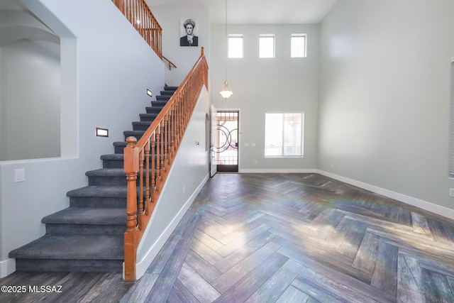 entryway with stairway, a towering ceiling, baseboards, and arched walkways
