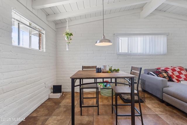 dining space with vaulted ceiling with beams and brick wall