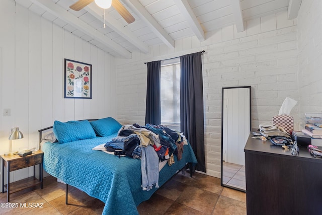 bedroom featuring a ceiling fan, beamed ceiling, and brick wall