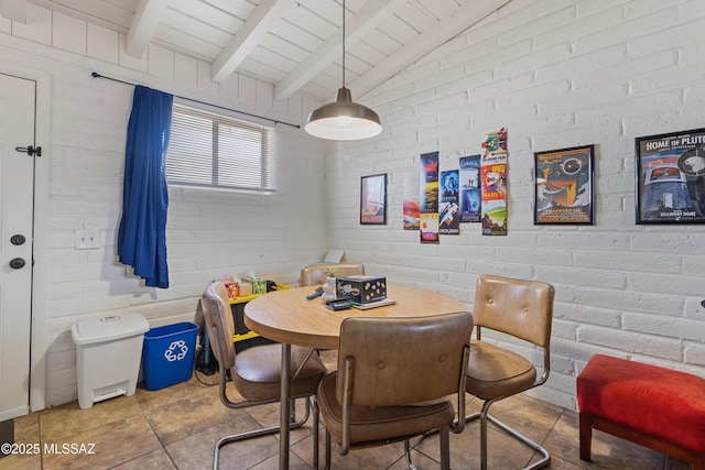 dining room featuring lofted ceiling with beams and brick wall