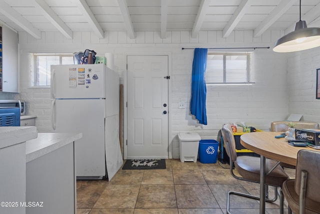 interior space featuring a healthy amount of sunlight, beam ceiling, and freestanding refrigerator