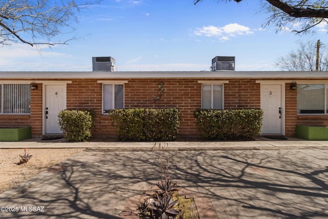 view of front of property with central air condition unit, a chimney, and brick siding