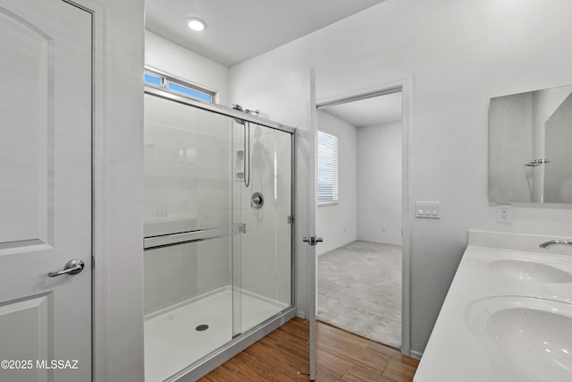 full bath with double vanity, a stall shower, wood finished floors, and a sink