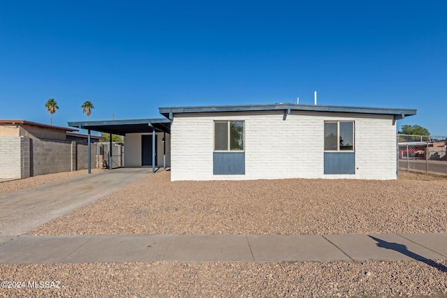 view of front facade featuring driveway, brick siding, fence, and an attached carport