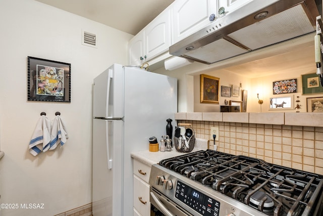 kitchen featuring visible vents, under cabinet range hood, decorative backsplash, freestanding refrigerator, and gas stove