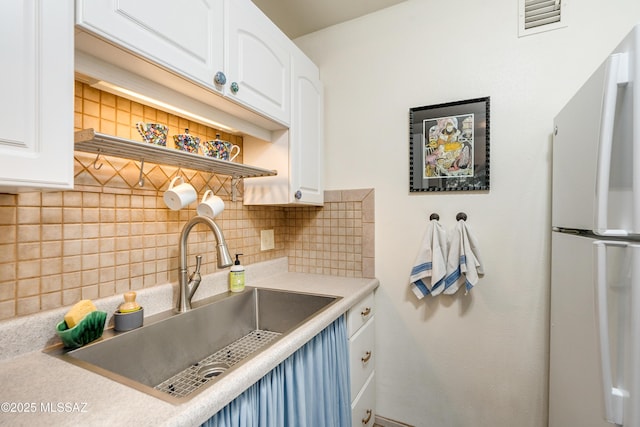 kitchen with a sink, backsplash, white cabinets, and freestanding refrigerator