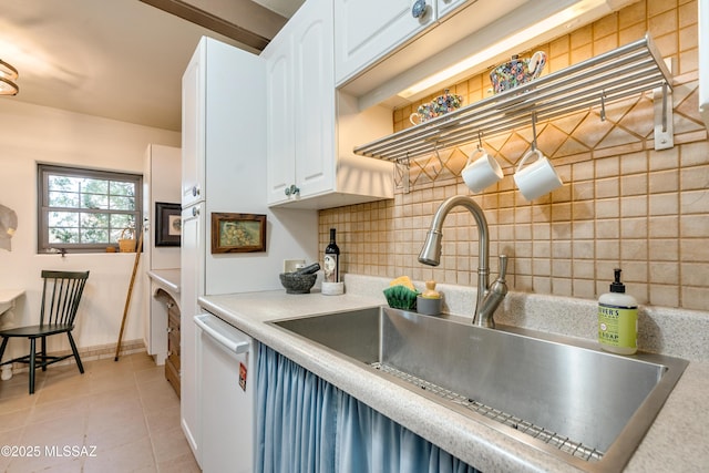 kitchen featuring tasteful backsplash, white dishwasher, light tile patterned flooring, white cabinetry, and a sink