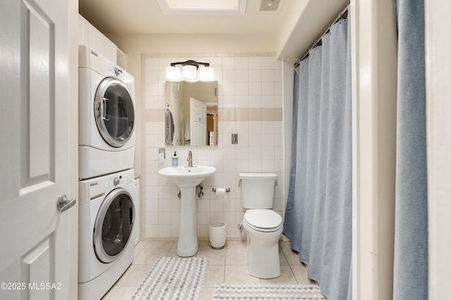 bathroom featuring visible vents, toilet, stacked washer and clothes dryer, tile patterned floors, and tile walls