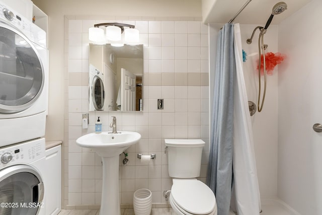 bathroom featuring a shower stall, stacked washer and dryer, toilet, and tile walls