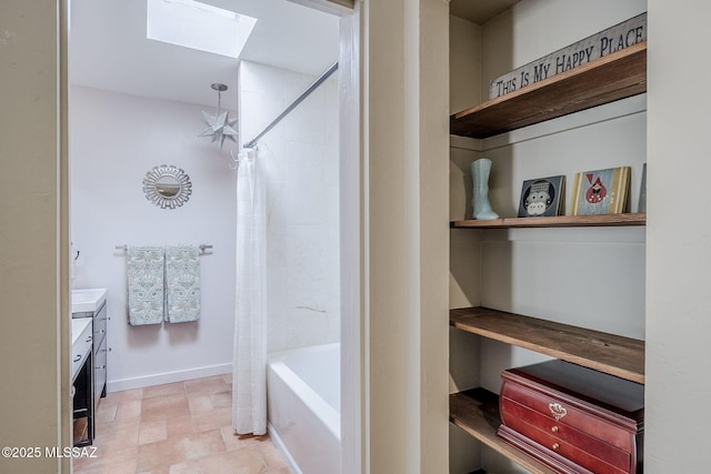 bathroom with a skylight, baseboards, shower / bath combination with curtain, and vanity