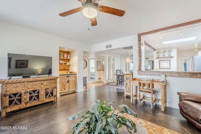 living room featuring a skylight, baseboards, visible vents, ceiling fan, and dark wood-style flooring