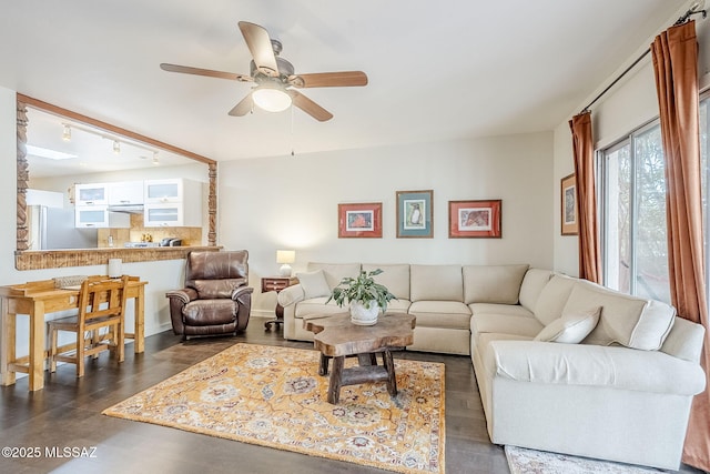 living area featuring rail lighting, a ceiling fan, and baseboards