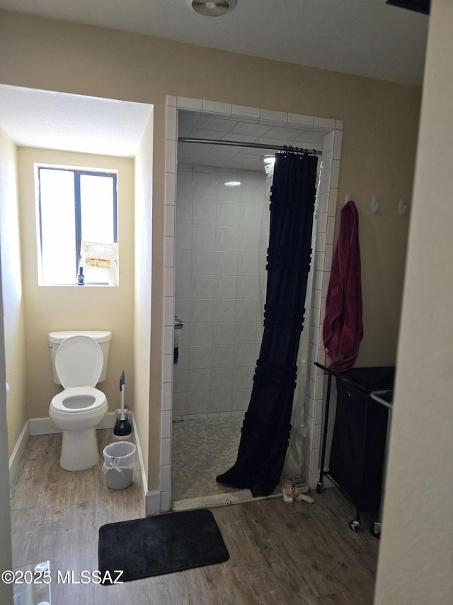 full bathroom with a tile shower, toilet, and wood finished floors