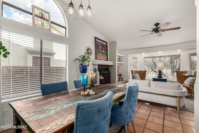 dining area with vaulted ceiling, a warm lit fireplace, plenty of natural light, and ceiling fan