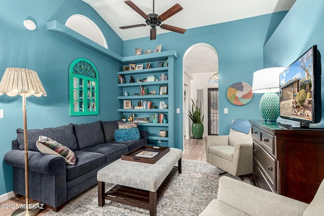 tiled living room featuring arched walkways, ceiling fan, high vaulted ceiling, and baseboards