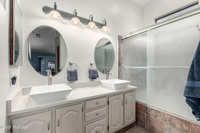 bathroom featuring double vanity, visible vents, a sink, and a shower with shower door