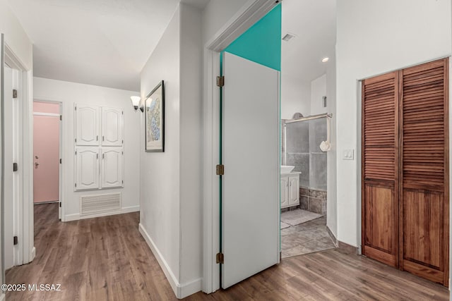 corridor with baseboards, visible vents, and wood finished floors