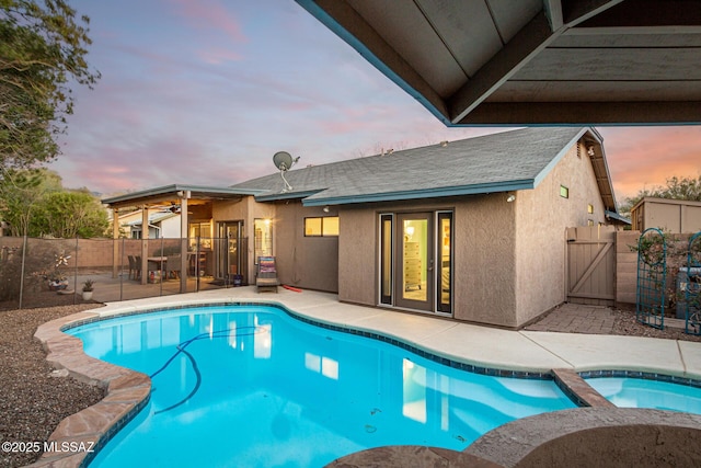 pool at dusk featuring a patio area, a fenced backyard, and a pool with connected hot tub