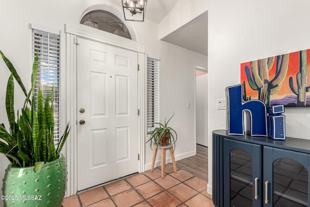 entrance foyer featuring light tile patterned flooring, a notable chandelier, and baseboards