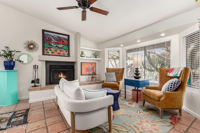 living area with a warm lit fireplace, vaulted ceiling, baseboards, and ceiling fan