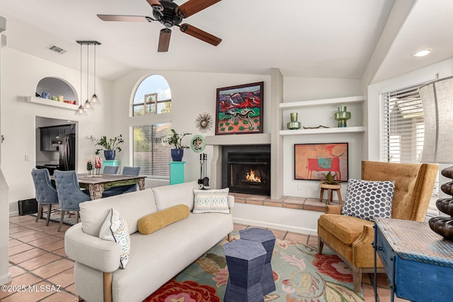 living area with built in features, lofted ceiling, visible vents, and a lit fireplace