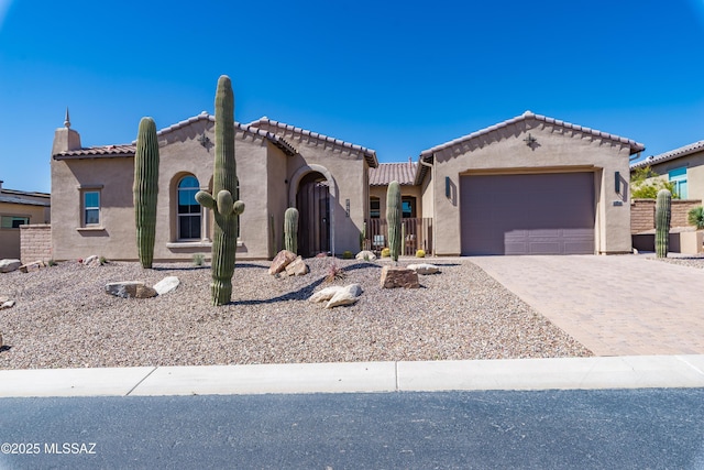 mediterranean / spanish-style house featuring decorative driveway, fence, an attached garage, and stucco siding