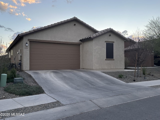 view of front of property featuring a garage, concrete driveway, a tiled roof, and stucco siding