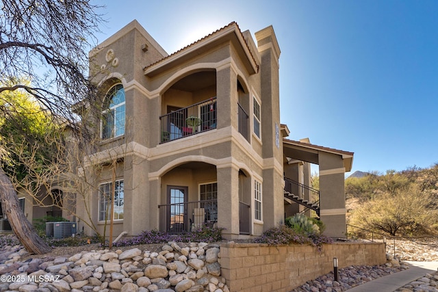 view of front of home with central AC, a tile roof, a balcony, and stucco siding