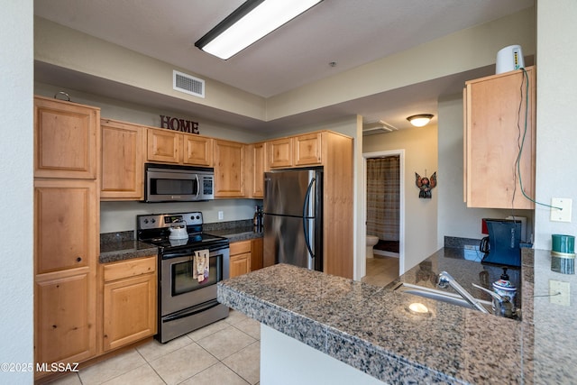 kitchen featuring light tile patterned flooring, stainless steel appliances, a peninsula, a sink, and visible vents