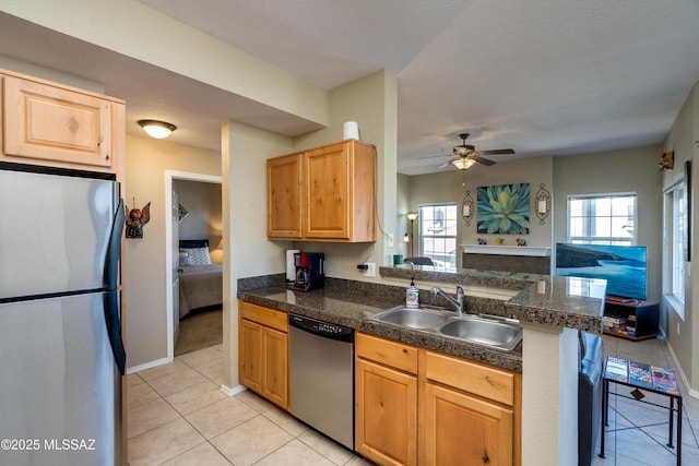 kitchen with tile countertops, a peninsula, a sink, open floor plan, and appliances with stainless steel finishes