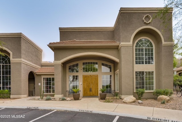 property entrance featuring a tile roof, uncovered parking, and stucco siding