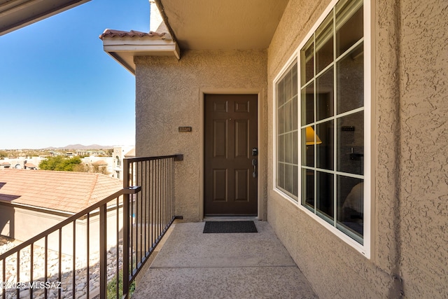 view of exterior entry featuring a tile roof, a balcony, and stucco siding